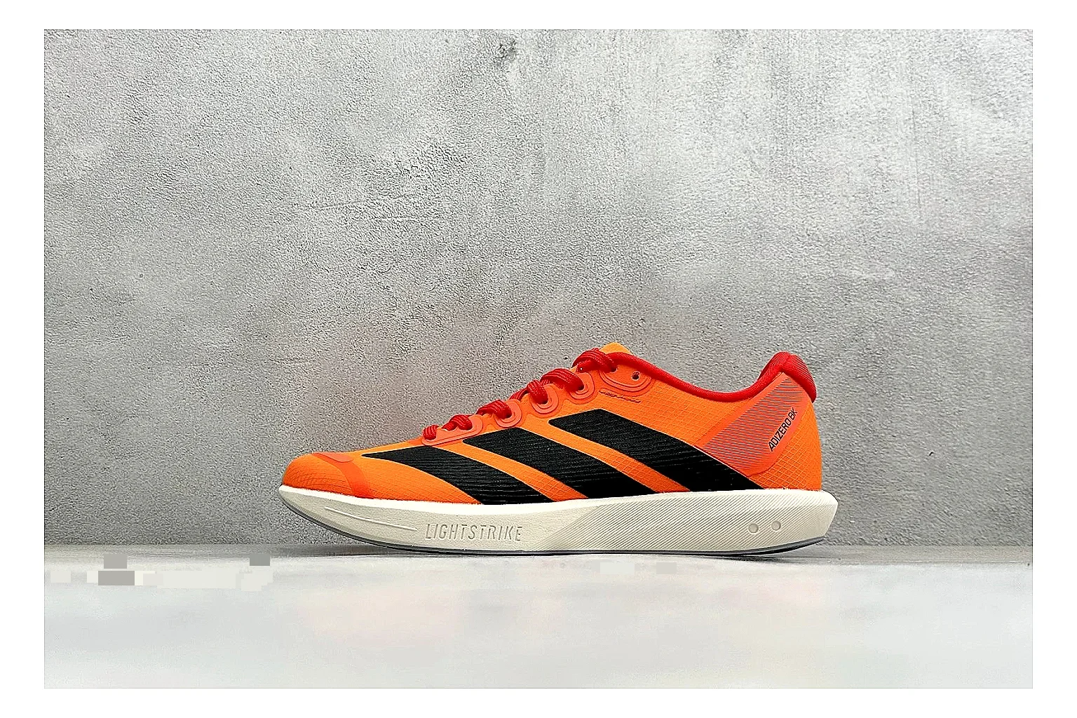 Adidas Adizero Orange Black QC reference photo showing orange runner upper, black three-stripe contrast, lightweight racing shape, and thin performance sole